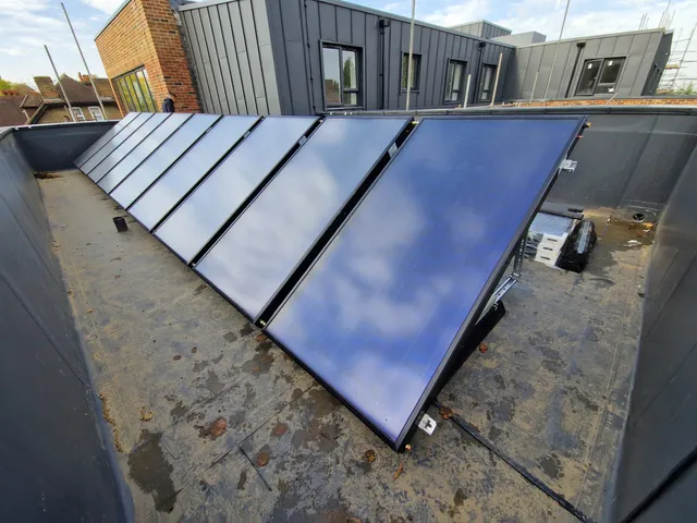 A row of flat-plate solar thermal collectors mounted on angled frames on a flat roof
